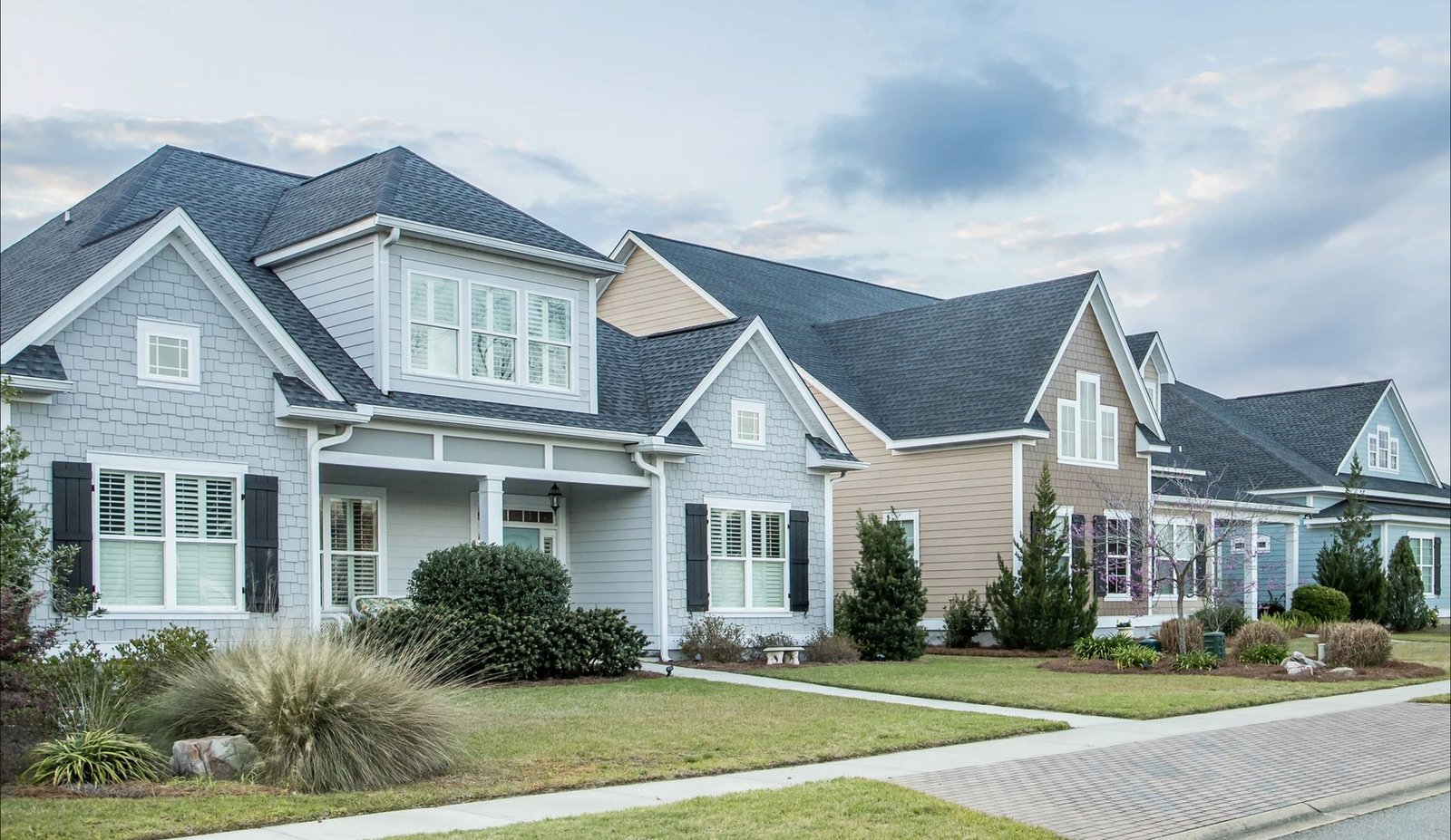 Row of suburban homes with pitched roofs under a partly cloudy sky
